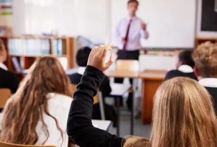 Teacher talking to student with her hand up in classroom