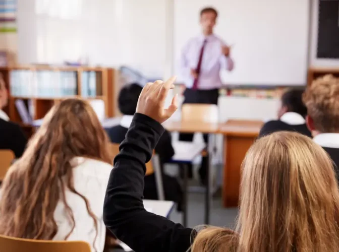 Teacher talking to student with her hand up in classroom