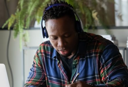A student wearing headphones, writing with a pen