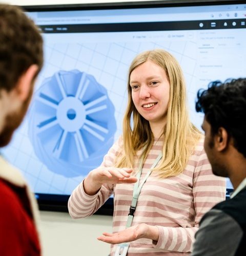 Young woman explaining technical drawing on screen behind her on screen to peers