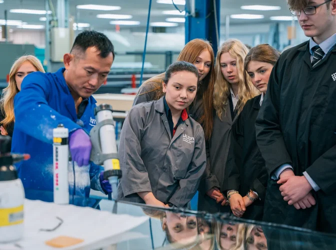 A technician using a solvent gun in a factory environment whilst students observe